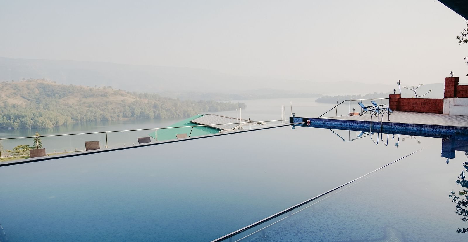 An image of the infinity waterfall swimming pool with a lake and mountain view in the background - Nisarga Lake Resort