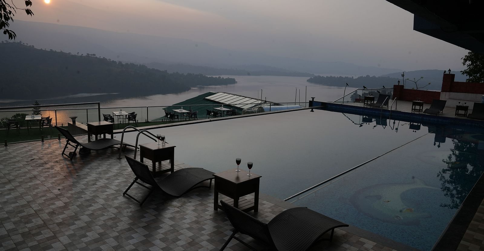 An image of the infinity waterfall swimming pool with lounge chairs placed beside it - Nisarga Lake Resort