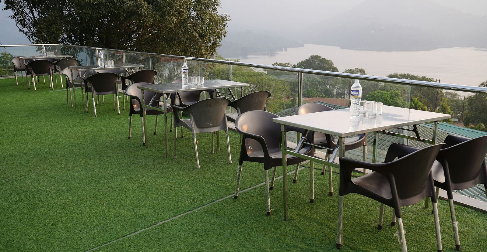 An image of the Lake View Oasis restaurant with chairs and tables at the rooftop and mountains and lake view in the background - Nisarga Lake Resort