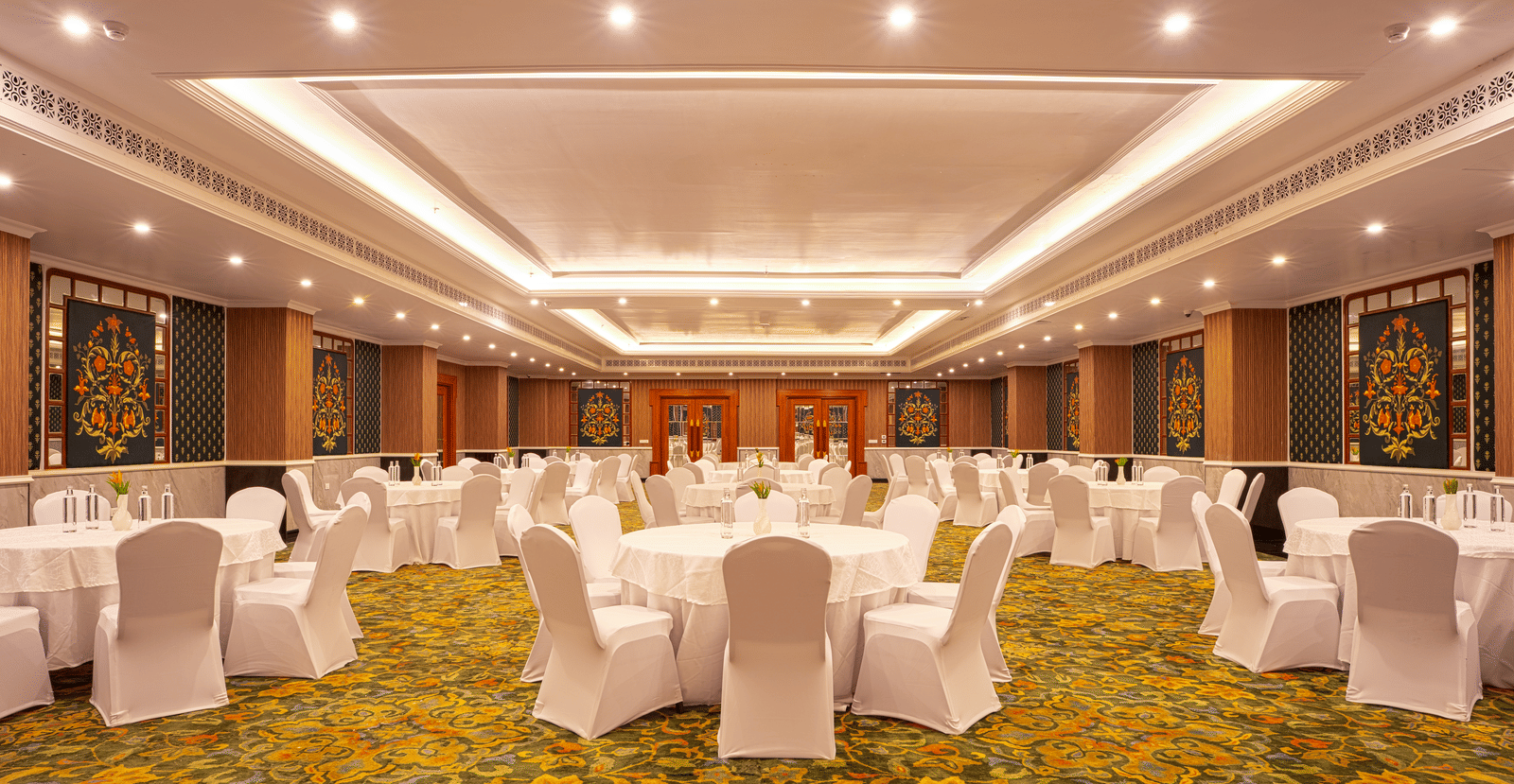A large, elegant banquet hall with a patterned yellow carpet, set up with multiple circular tables and chairs at MAYFAIR Bay Resort, Paradeep.