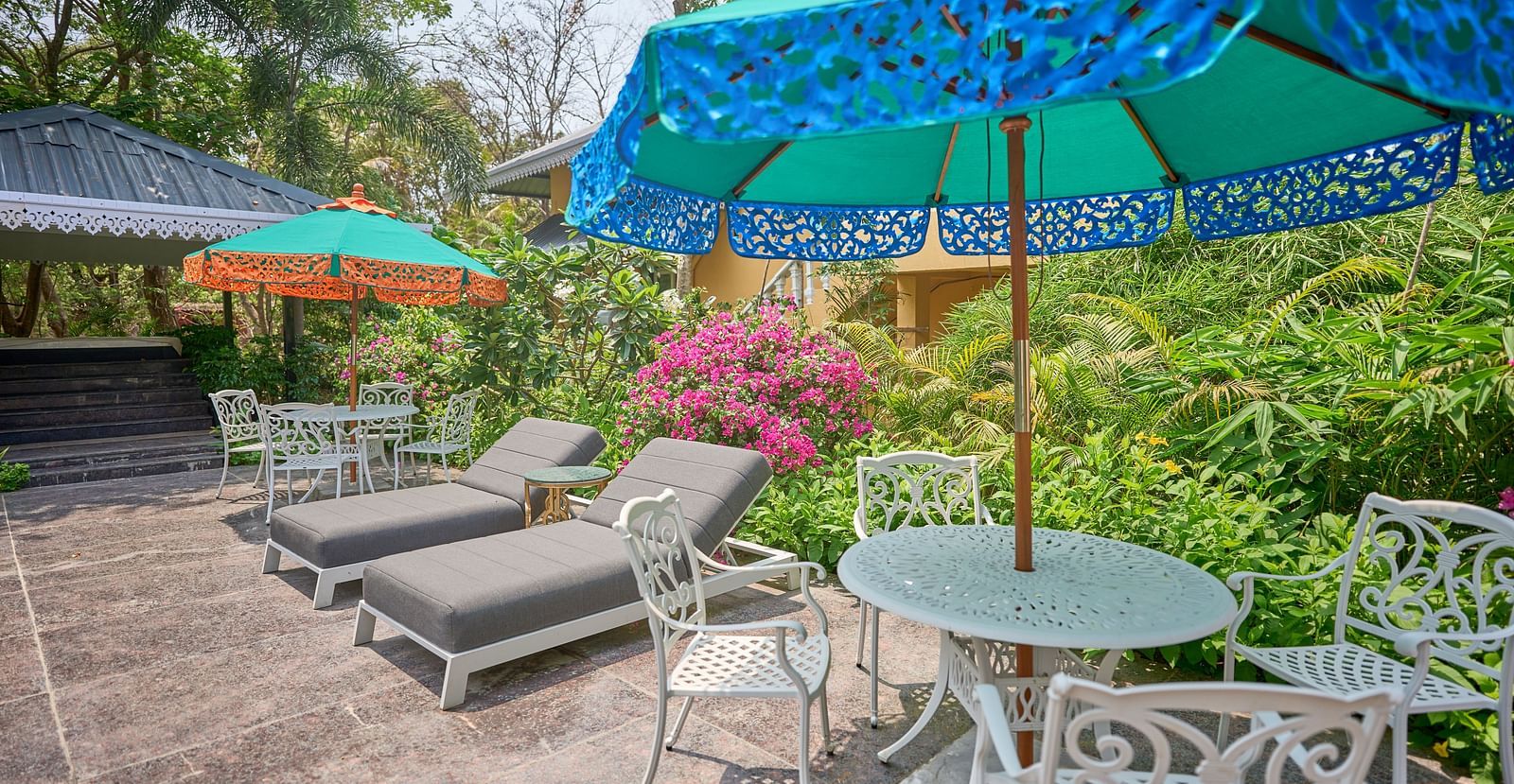 Lounger chairs and an umbrella placed over the table, with plants and trees in the background at Mayfair Manor, Alibag