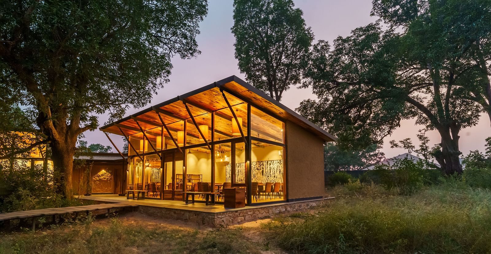 Facade view of a well lit cottage surrounded by trees at Trees N Tigers, Tadoba.