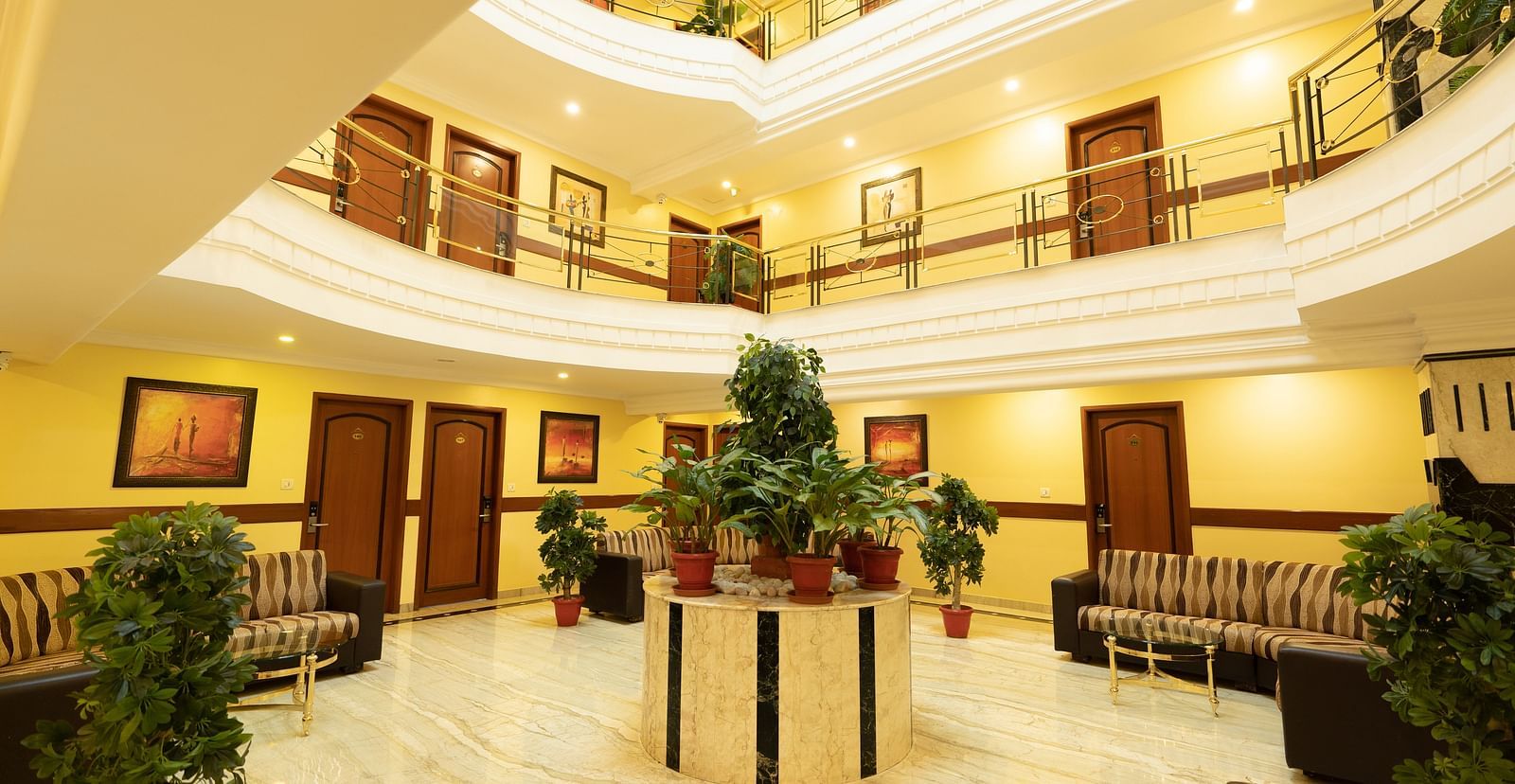 An image of interiors of a multi storey hotel which has a lobby in ground floor with plants  and seating area - Pai Group of Hotels
