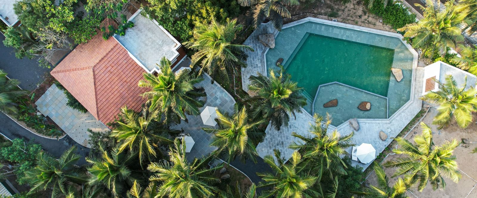  An aerial view of a resort with a swimming pool, surrounded by palm trees and lush greenery.
