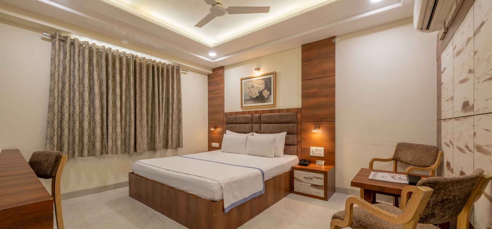 A well furnished spacious room with a king size bed, wooden furniture, and elegant curtains at Hotel Highway King, Jaipur.