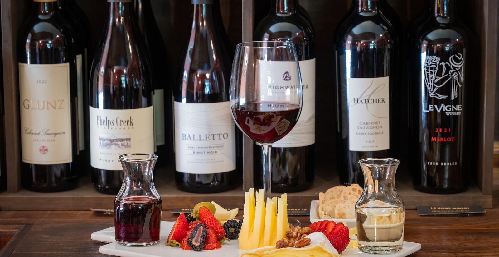 Wine bottles and a cheese platter with fruit displayed on a wooden table at The Groveland Hotel.