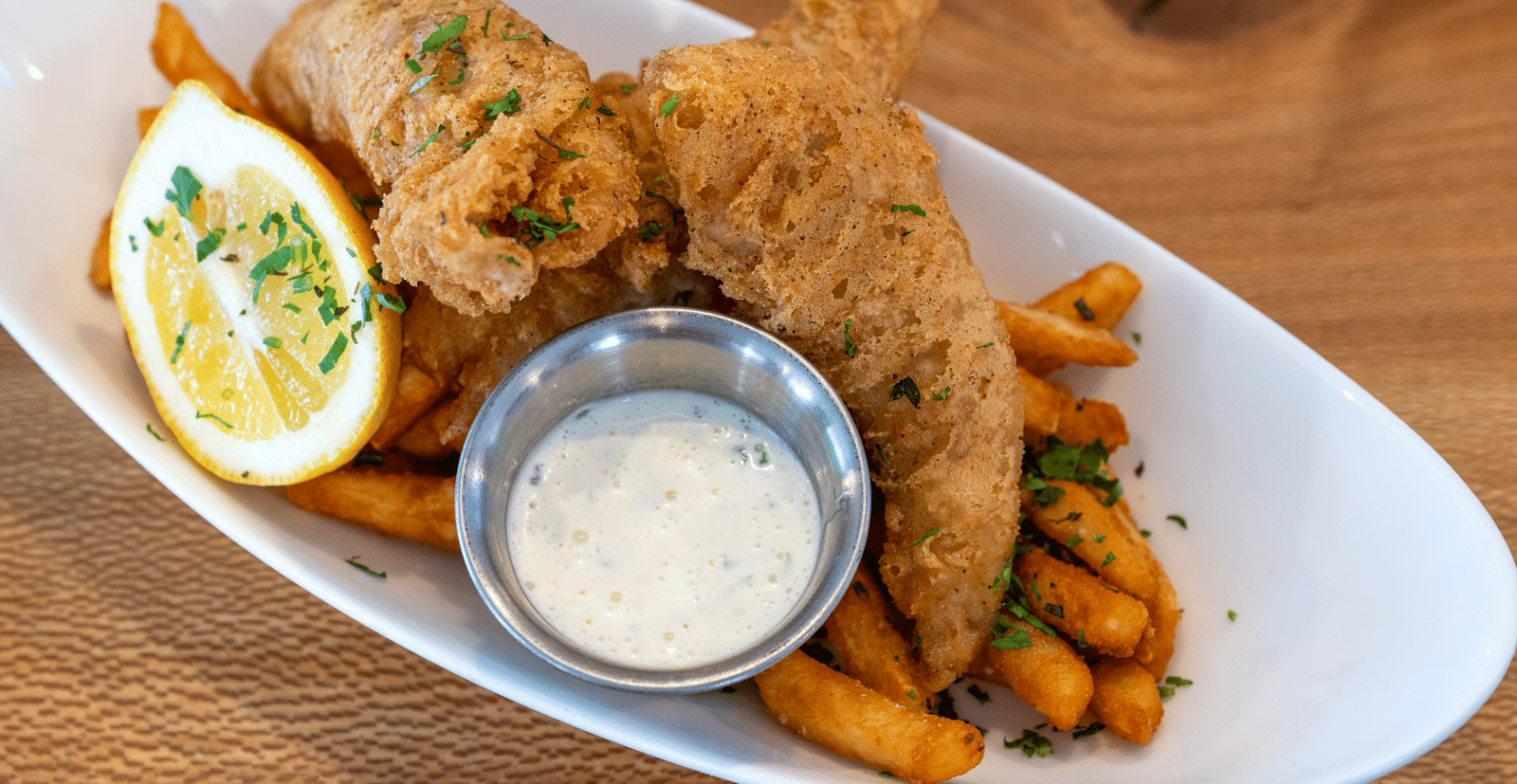 Crispy fried fish and chips with tartar sauce and lemon wedge served with seasoned fries at The Groveland Hotel.