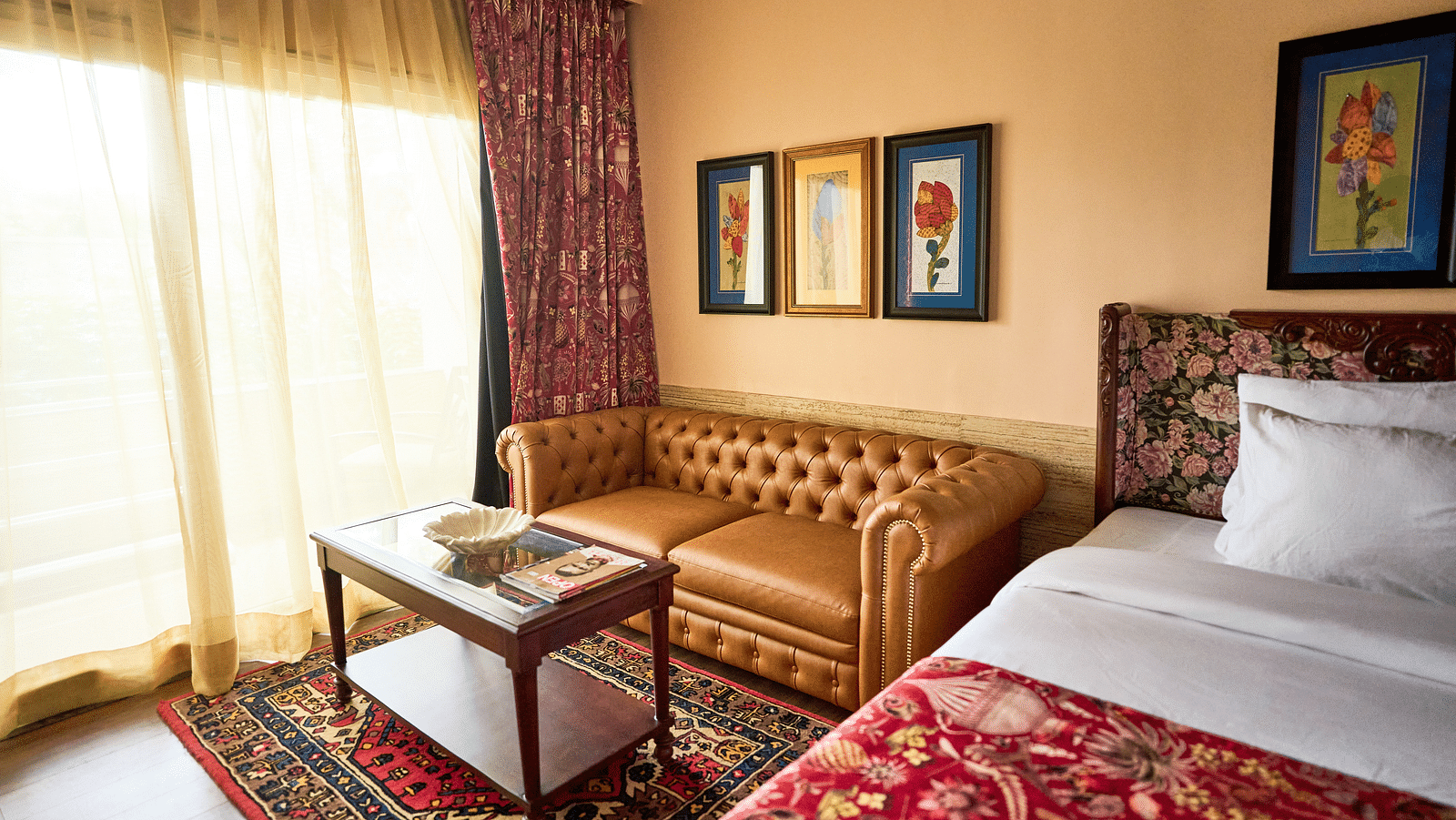 A spacious room featuring a bed on one side, a cushioned sofa on the other, and a glass table near the window adorned with closed curtains at Mayfair Manor, Alibag