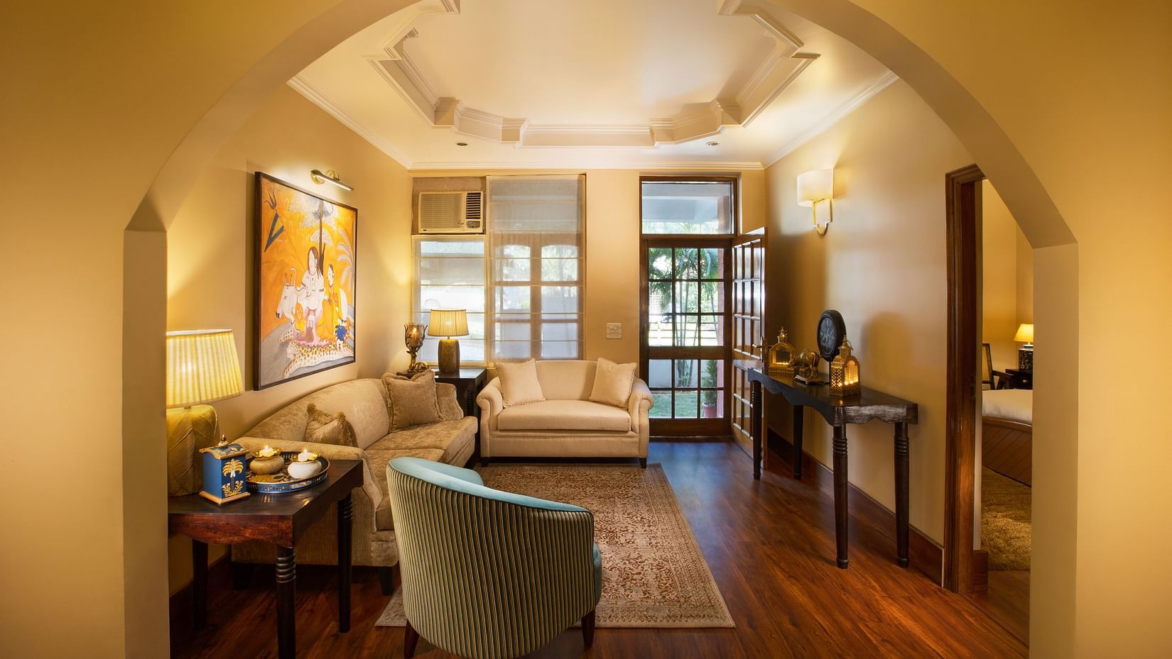 An image of a living room features comfy sofas, large windows, wall paintings, and other decorative items - Lamrin Boutique Cottages Rishikesh