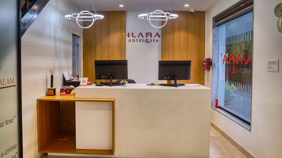The well-lit and modern reception desk, featuring two computer monitors and clean wooden accents at Ilara Hotels & Spa, OMR, Chennai.