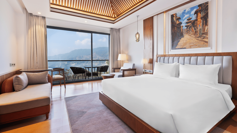 Premium Room bedroom at Royal Tulip Shivapuri National Park - Kathmandu featuring a king bed, a sofa, and a balcony with a view of the mountains.