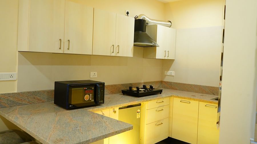 A kitchen with a microwave, a cooking stove, a chimney and storage cabinets - A M Suites