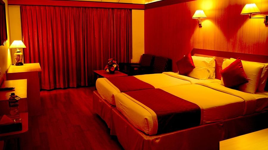  Hotel Yasodha Towers - Interior view of a bedroom featuring a double bed, wooden flooring and red curtains in yellow ambient lighting