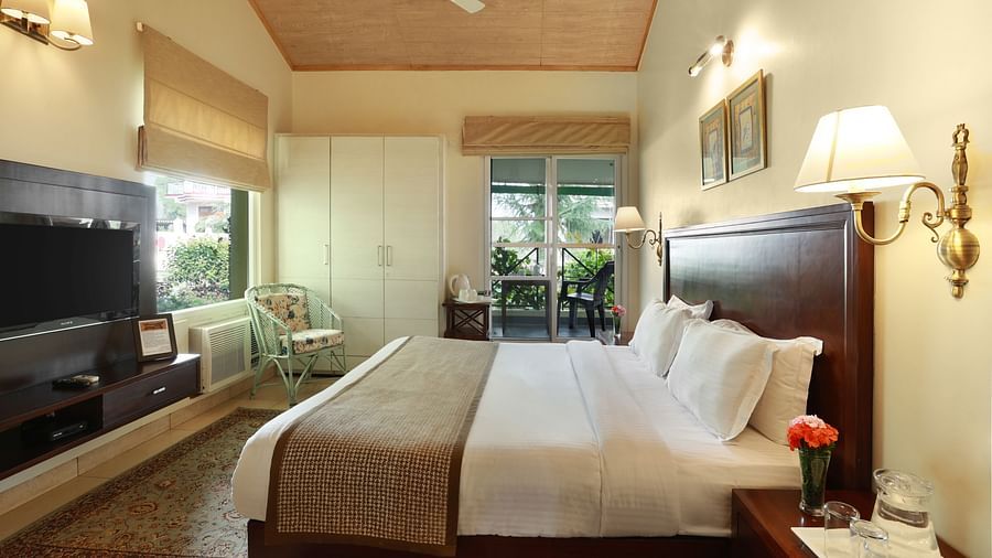 A grand room with a cosy setting showcasing windows with serene view and amenities like bedside lamps, a television, a wardrobe, etc. - Lamrin Norwood Green, Palampur