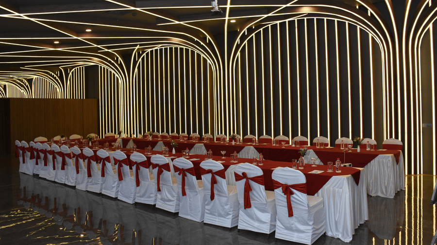 A banquet hall at Comfort Inn Sapphire by Eastlynn Collections, Jaipur with rows of cloth covered chairs, a table, and patterned wall design.