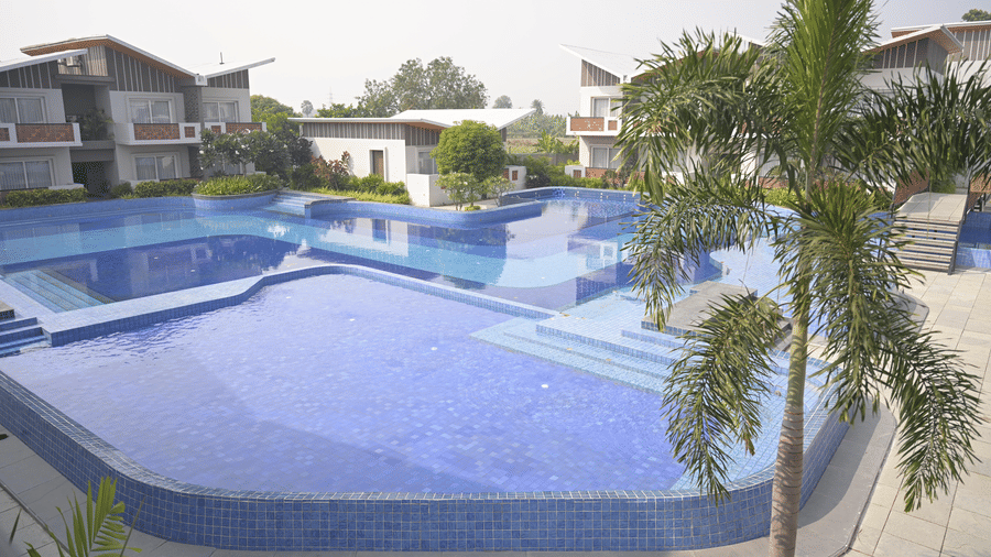 A wide view of the Hotel Sonar Bangla, Mayapur swimming pool surrounded by palm trees.