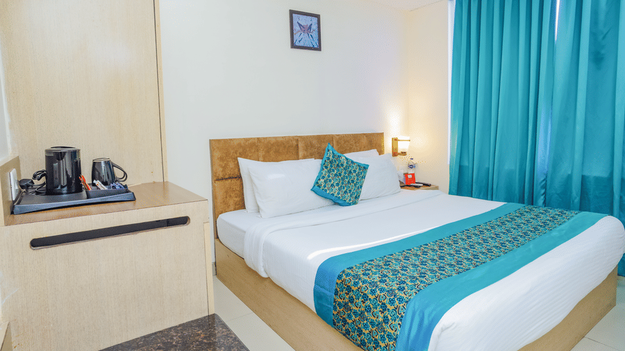 A hotel room with a double bed, a vibrant blue bed runner, and a wooden headboard - Hyphen Grand, Haridwar