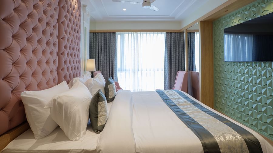 A modern hotel room features a bed with white linens and a television mounted on the wall - Melior Inn