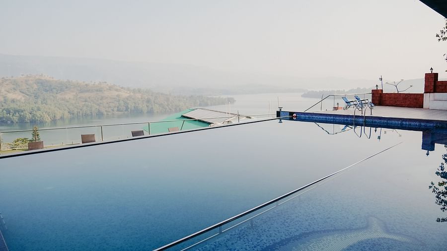 An image of the infinity waterfall swimming pool with a lake and mountain view in the background - Nisarga Lake Resort