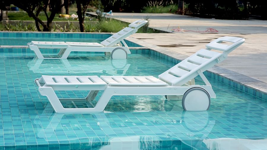 White sun loungers partially submerged in a turquoise pool, surrounded by trees and a stone deck at Wyndham Garden.