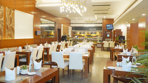 A side angle view of the restaurant interior at Nemesia featuring chandeliers, wooden furniture, tables arranged with napkins, water glasses, and plates.