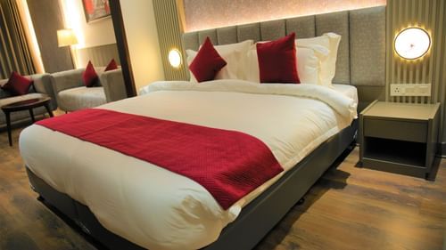 Suite room with large bed and red linens at Pride Biznotel Haldwani featuring a sitting space in the background