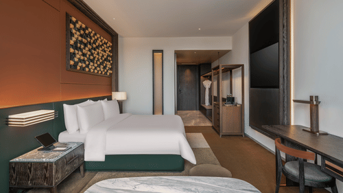 Side view of the Premium King room at The Residency Signature Madurai with a king bed, wall-mounted TV, wooden panelling, and warm ambient lighting.