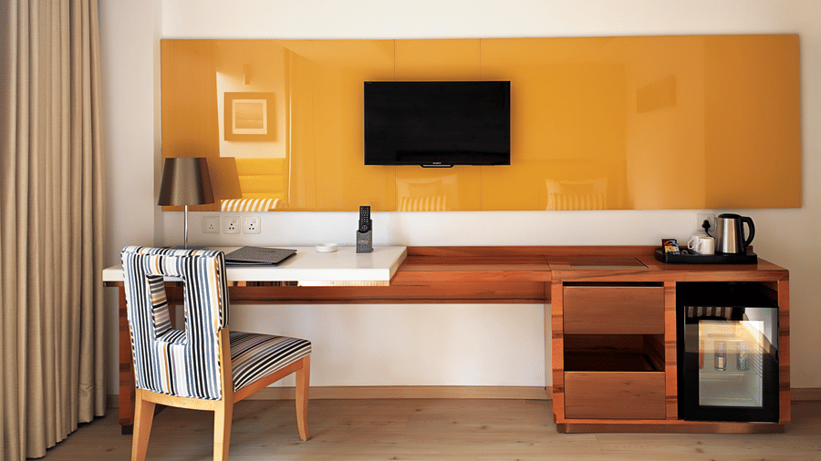 The workspace in a Deluxe Room at Barsana Boutique Hotel, Kolkata, with a work desk, chair, television, minibar, and a tea/coffee station.