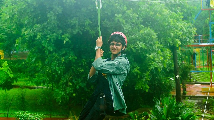A charming teenager wearing a helmet on a zipline, with the backdrop of a huge tree's canopy