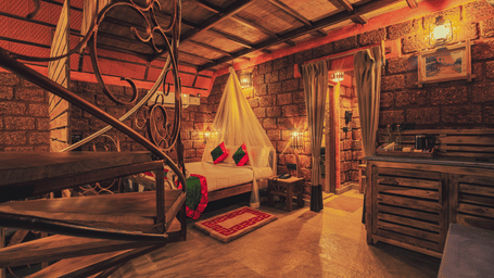 An Oak Premium Cottage in Coorg at Copper Edge - Eco Resort in a rustic setting, featuring a plush bed next to a nightstand facing a spiralling staircase.