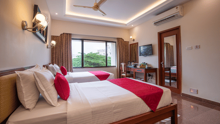 A modern Premium Room with twin beds, a large window with curtains, a ceiling fan, TV, desk, and wall-mounted lights