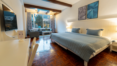 A spacious premium suite featuring light blue bedding, wall-mounted TV, and bright natural light - Johnson Lodge & Spa, Manali