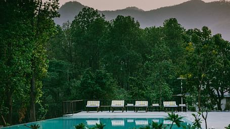 A view of the outdoor swimming pool at Saraca Resort & Spa Corbett surrounded by lush trees and mountains