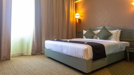A guest room at Shilton International, Kochi, featuring a large bed, and a window with natural light.