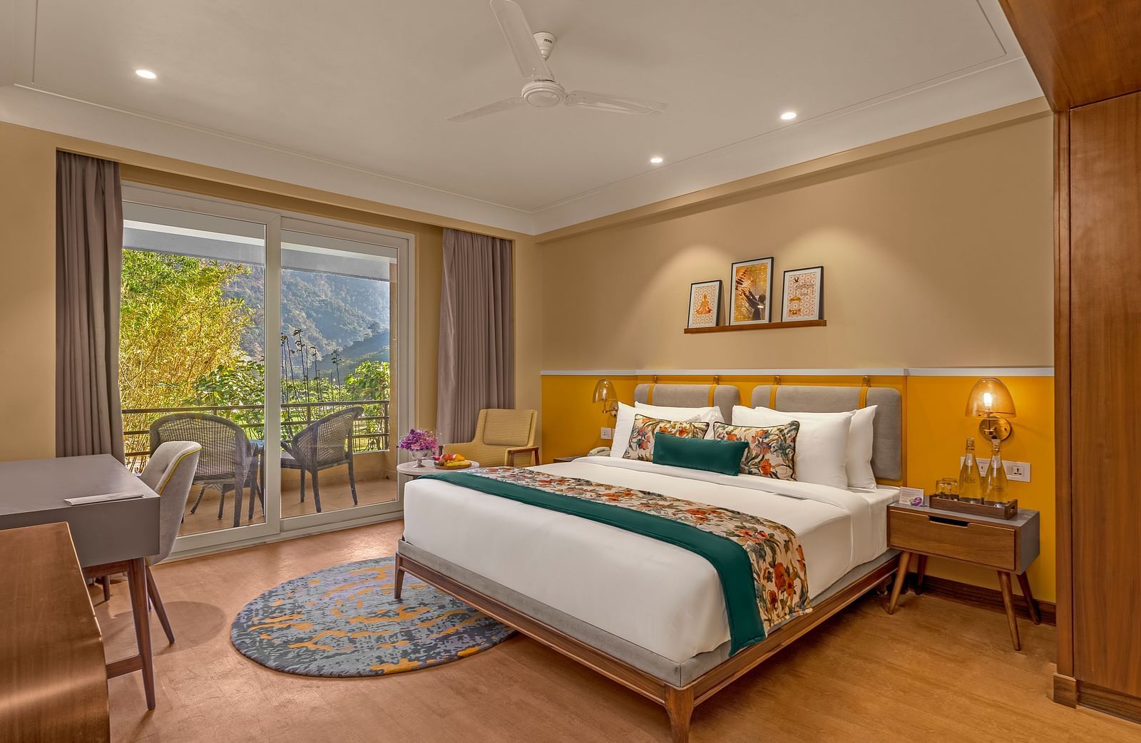 Image of a  room features a large king-size bed with a plush headboard and comfortable bedding. A comfortable armchair sits by a large window offering breathtaking views. The room also includes a wooden desk with a chair, a television, and a ceiling fan. T