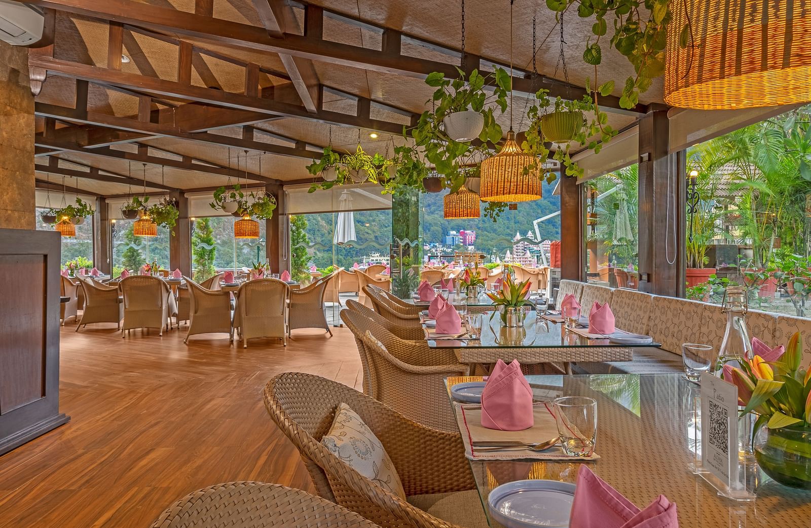 A spacious restaurant with a wooden floor and exposed wooden beams on the ceiling. Large windows offer views of the outdoors.