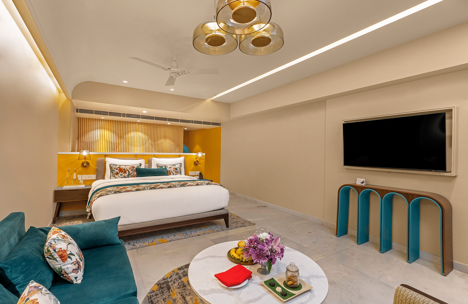 A n image of luxurious hotel suite with king bed, sofa, coffee table, and stylish decor.