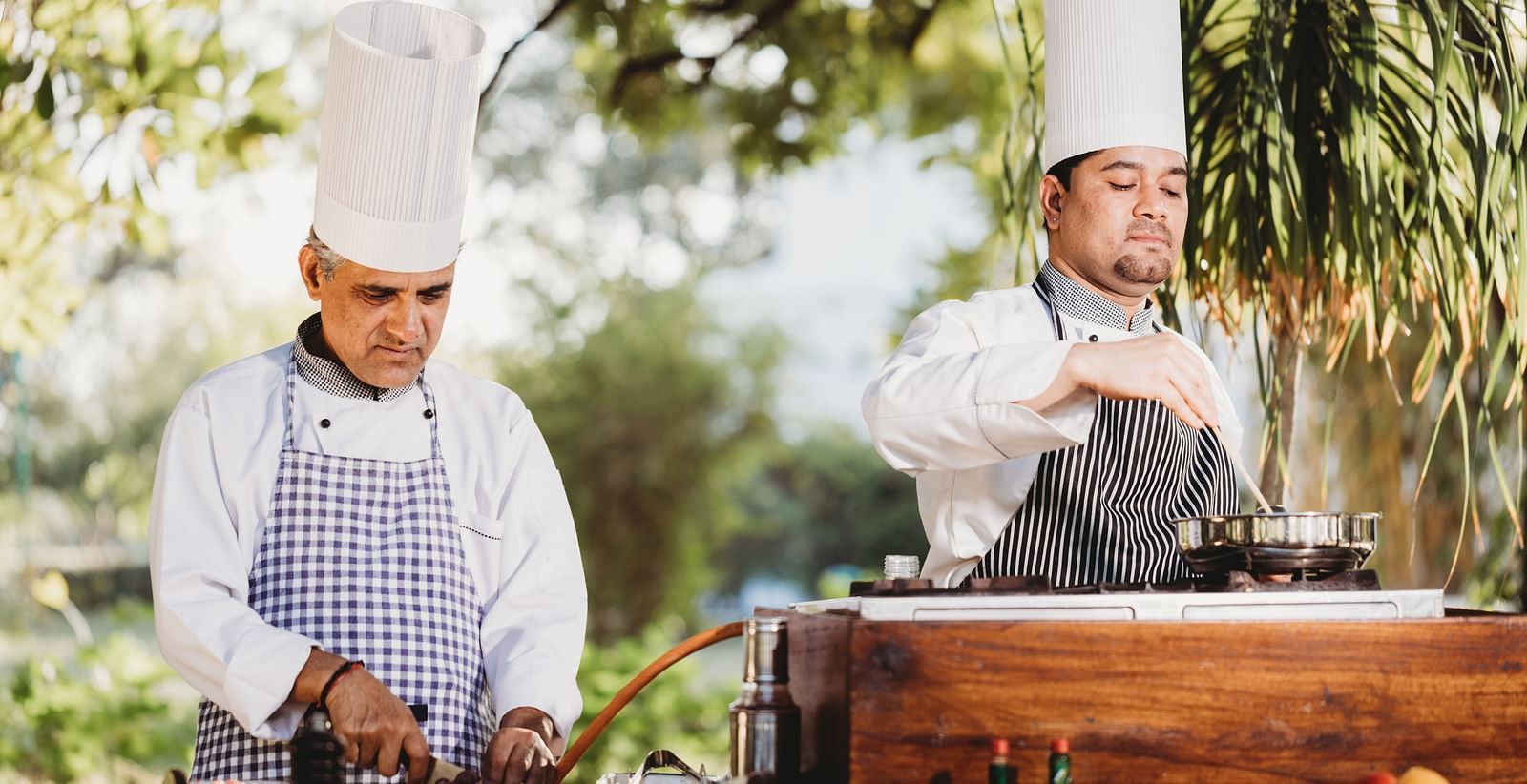 Two men with chef's hat cooking with a big stove in front of them- Shahpura Bagh.