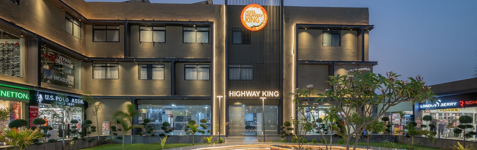 Facade and well-manicured lawn of Hotel Highway King, Behror, which also features a large illuminated logo of the property.