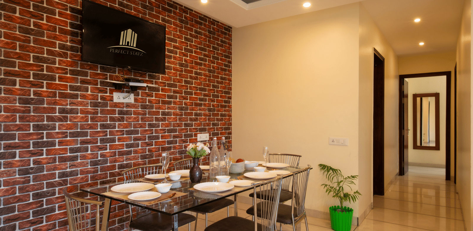 A dining area with a brick wall, a wall-mounted television, a dining table, and chairs at Perfectstayzz Value Shimla (Namah Retreat).