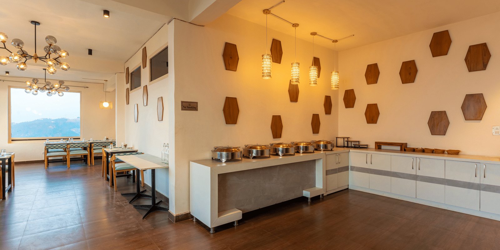 A long shot of the wide and brightly lit dining hall featuring unique geometric wall art at Himalayas Resort By The Lake Hill, Mukteshwar.