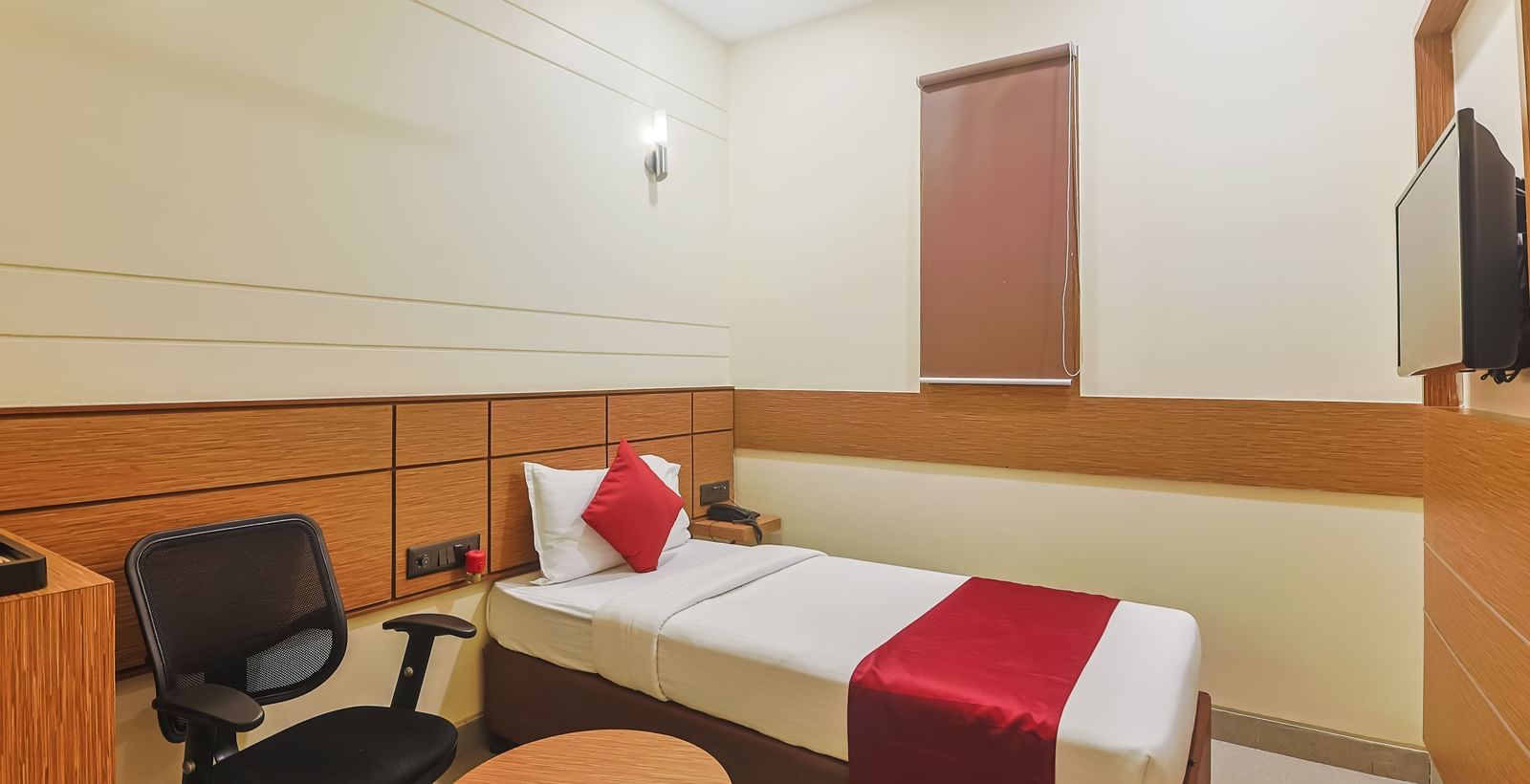 Bedroom with twin beds, red runners, pillows, chair and wall-mounted TV at Max Hotel Prayagraj.