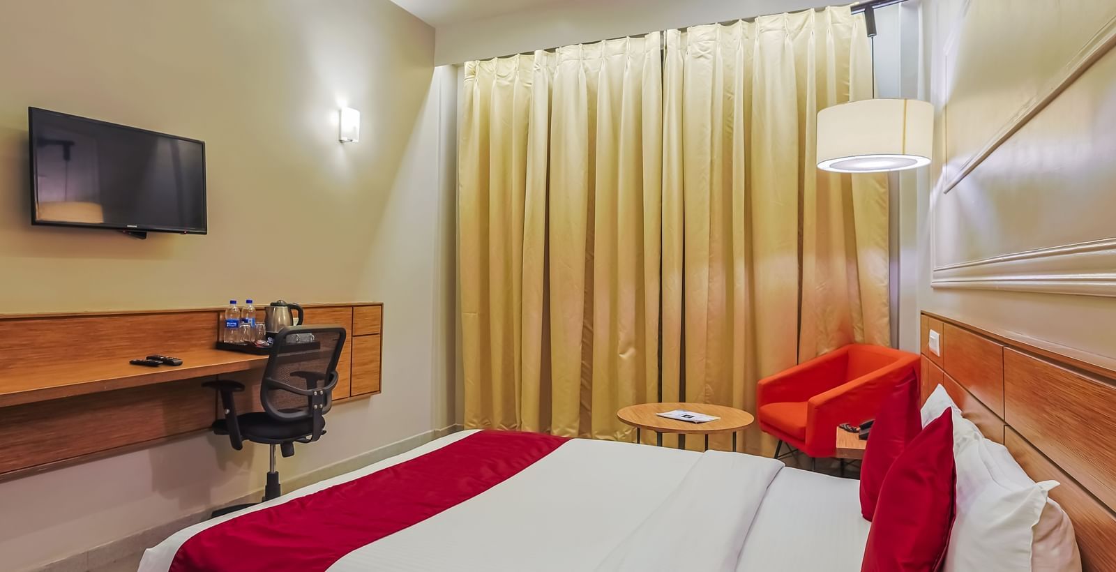 Bedroom with double bed, red runner, pillows, wall-mounted TV and curtains at Max Hotel Prayagraj.