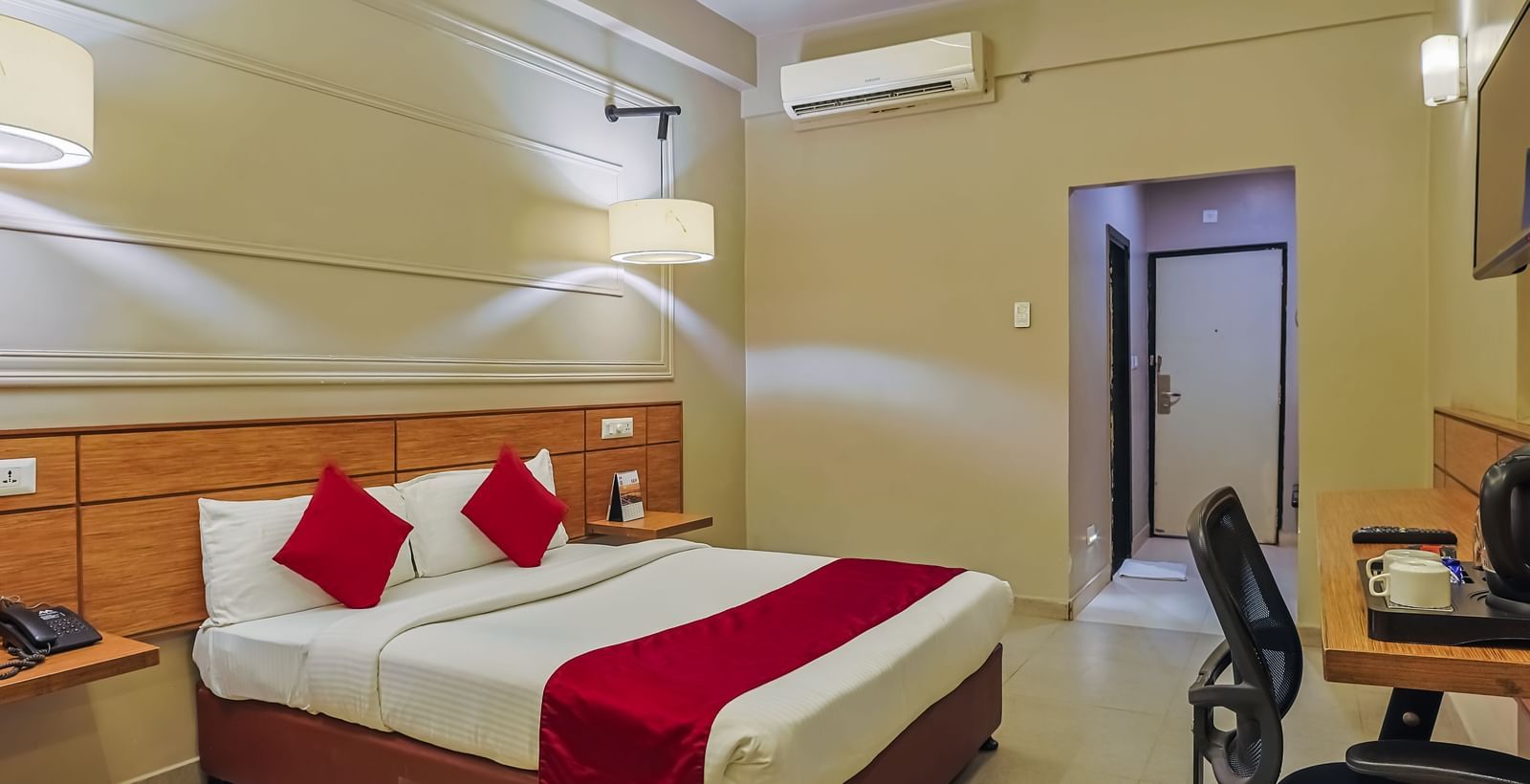 Bedroom with double bed, red runner, pillows, work desk and chair at Max Hotel Prayagraj.