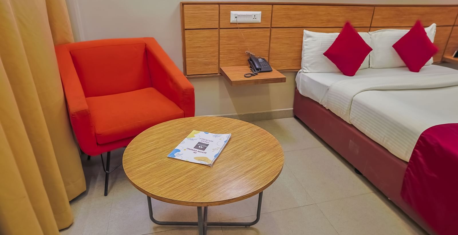 Seating area with orange chair, round table and bedside cabinet at Max Hotel Prayagraj.
