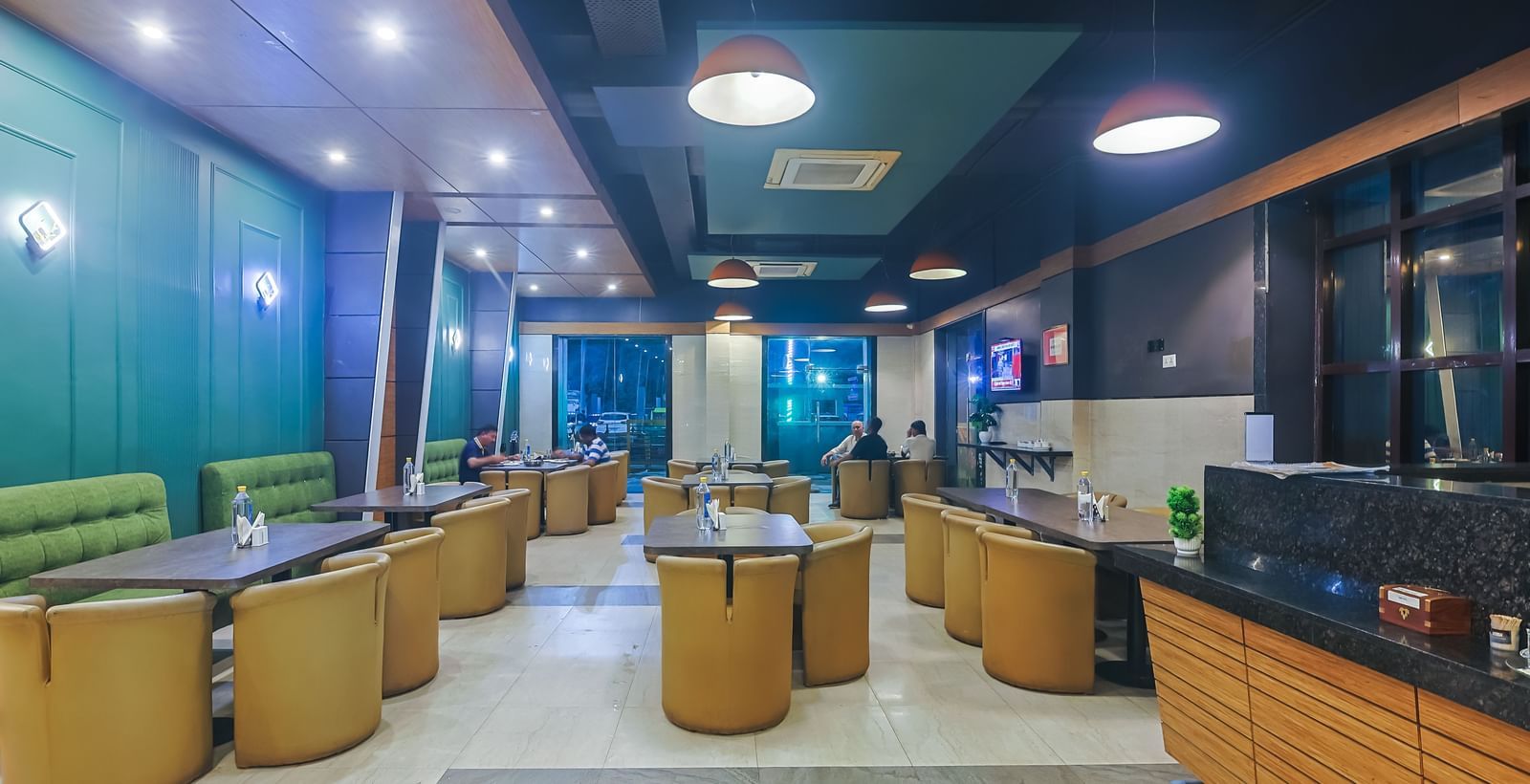 Restaurant with multiple dining tables, green accents and ceiling lights at Max Hotel Prayagraj.