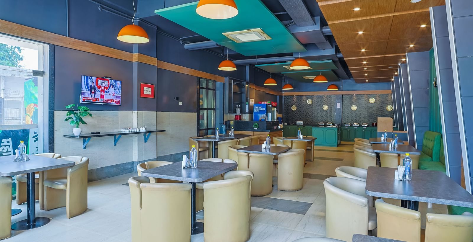 Restaurant with round tables, cushioned chairs and TV on wall at Max Hotel Prayagraj.