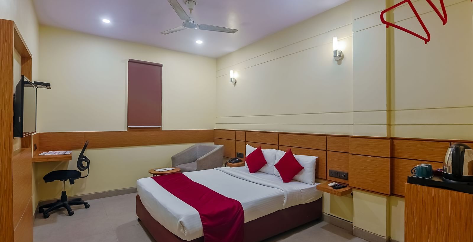 Bedroom with double bed, red runner, pillows, desk and wooden panel at Max Hotel Prayagraj.
