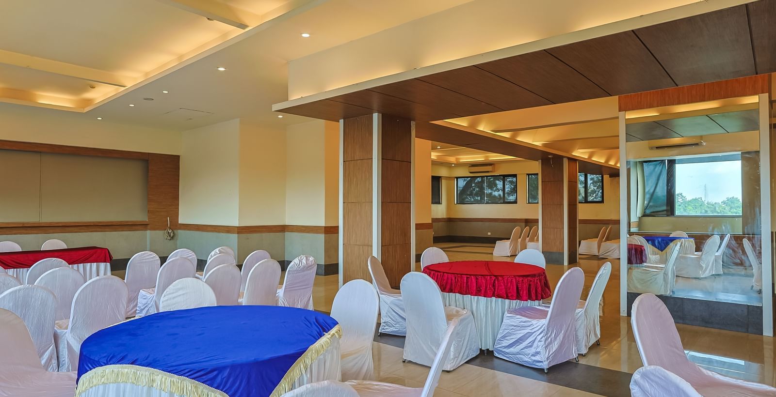 Banquet hall with round tables, white chairs and warm lighting at Max Hotel Prayagraj.