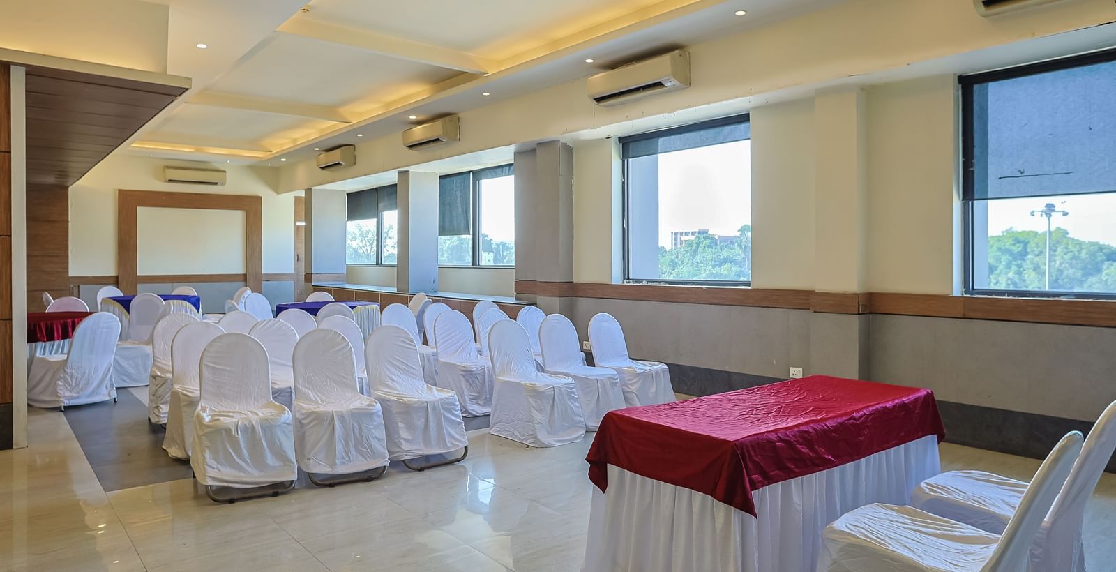 Banquet hall with rectangular tables, white chairs and large windows at Max Hotel Prayagraj.